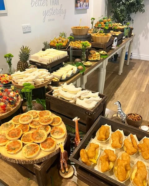 A jungle-themed baby shower food table with a tiered display of finger foods on dark wooden crates and platters.