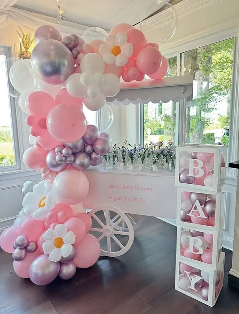 A white dessert cart decorated with a large pink and white balloon garland featuring stylized balloon daisies for a modern wildflower baby shower theme.