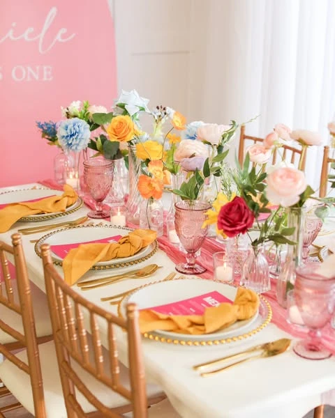 A long dining table set for a spring bridal shower with a vibrant color scheme of pink, orange, and yellow florals and gold accents.