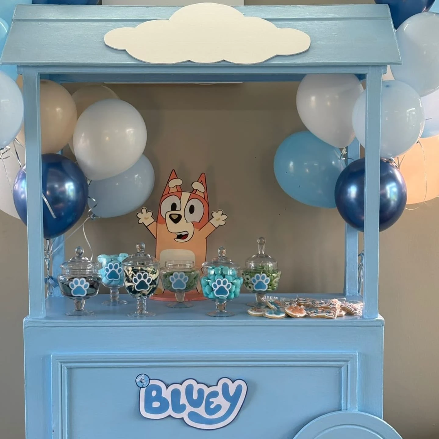 A light blue candy cart decorated with a Bingo cutout and glass jars filled with themed candies for a Bluey party.