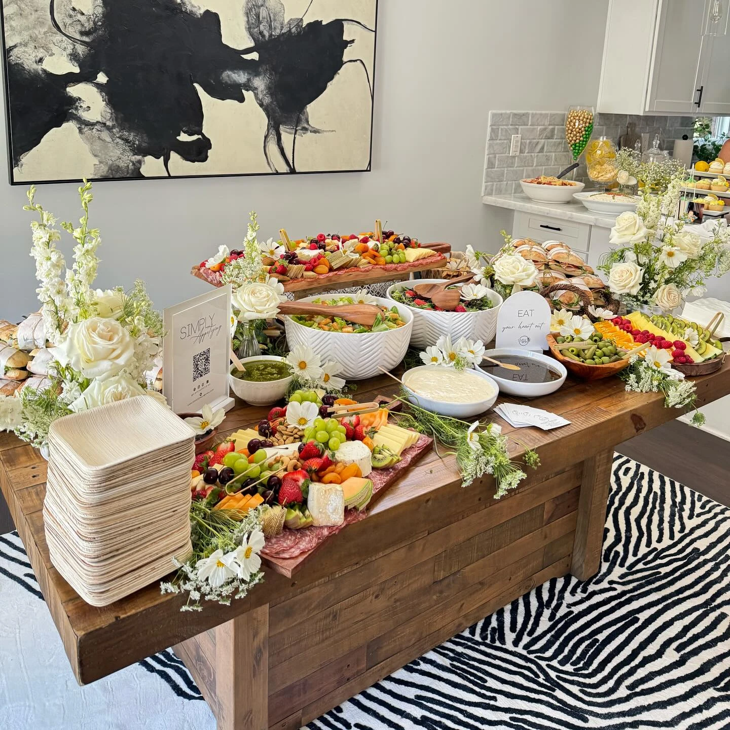 A long wooden table set up as a baby shower food buffet with charcuterie boards, salads, and fruit platters.