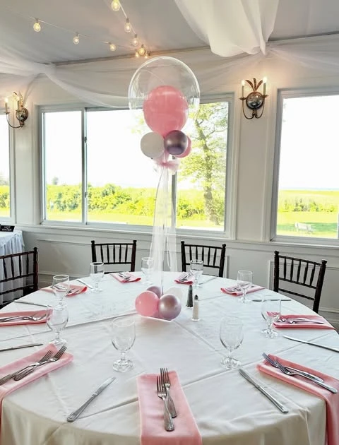 A round dining table with a tall, generic pink balloon centerpiece that does not match the wildflower theme.