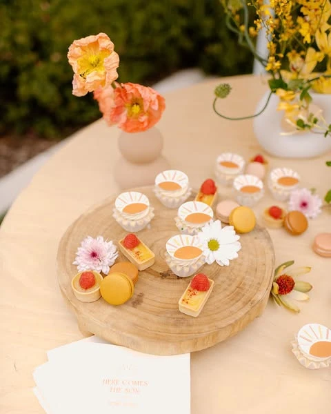 Sun-themed baby shower desserts, including macarons and tarts, displayed on a wooden platter.