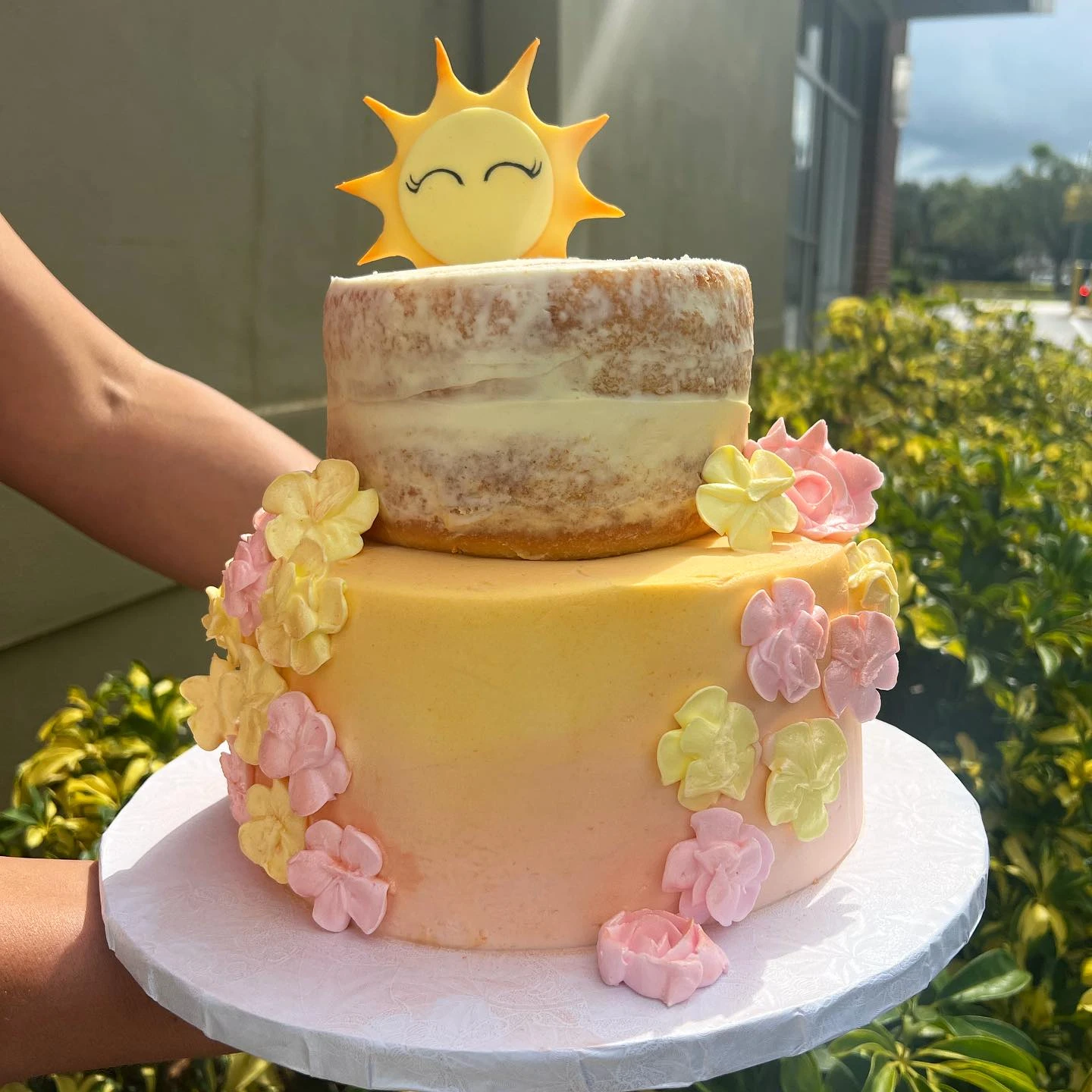 A two-tier 'you are my sunshine' baby shower cake with a smiling sun topper.