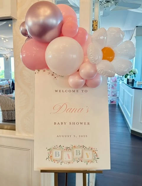A baby shower welcome sign decorated with a pink balloon cluster and a large white balloon daisy, demonstrating a mixed-media wildflower theme.