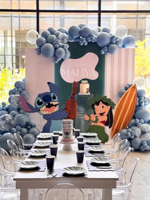 Wide view of a Stitch birthday party with a large character backdrop and blue balloon garland.