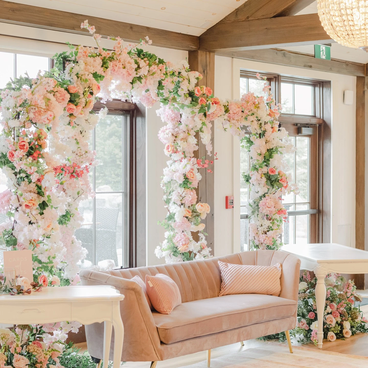 Pink floral arch photo backdrop with a pink velvet sofa for a spring bridal shower.
