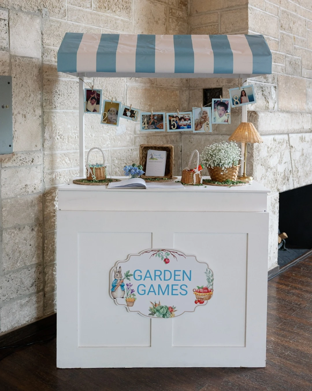 A white cart with a blue and white striped awning labeled 'Garden Games' for a Peter Rabbit baby shower.