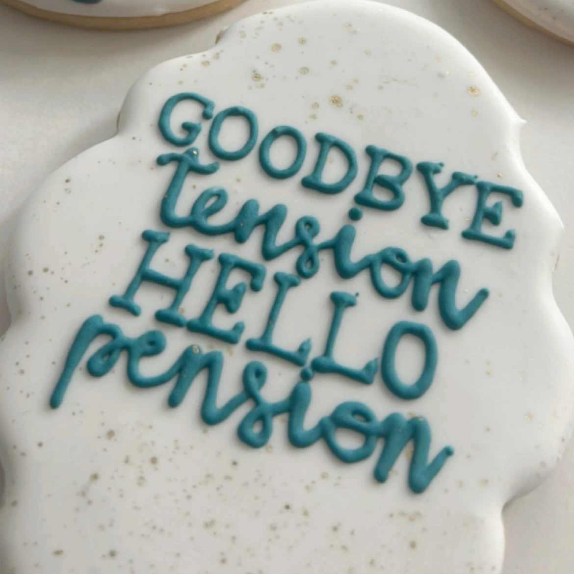 Funny retirement cookie that says 'Goodbye tension Hello pension' in teal script.