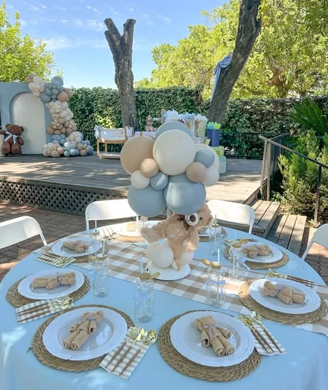 A baby shower table setting with a teddy bear centerpiece and small teddy bears on each plate.