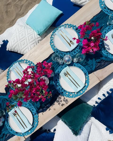Overhead view of a Mamma Mia bachelorette party tablescape with blue placemats, pink bougainvillea, and a mini disco ball.
