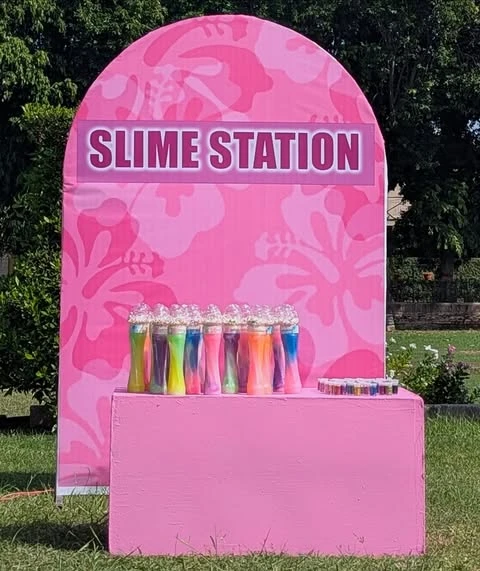 A pink 'Slime Station' with colorful slime party favors for a kids' party.