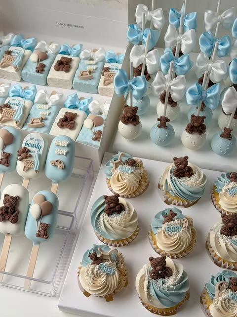 Assortment of 'we can bearly wait' baby shower desserts in a light blue, white, and brown color palette.