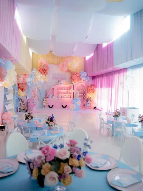 A wide view of a Bluey-themed birthday party decorated with pastel pink, blue, and yellow fabric draping on the walls and ceiling.