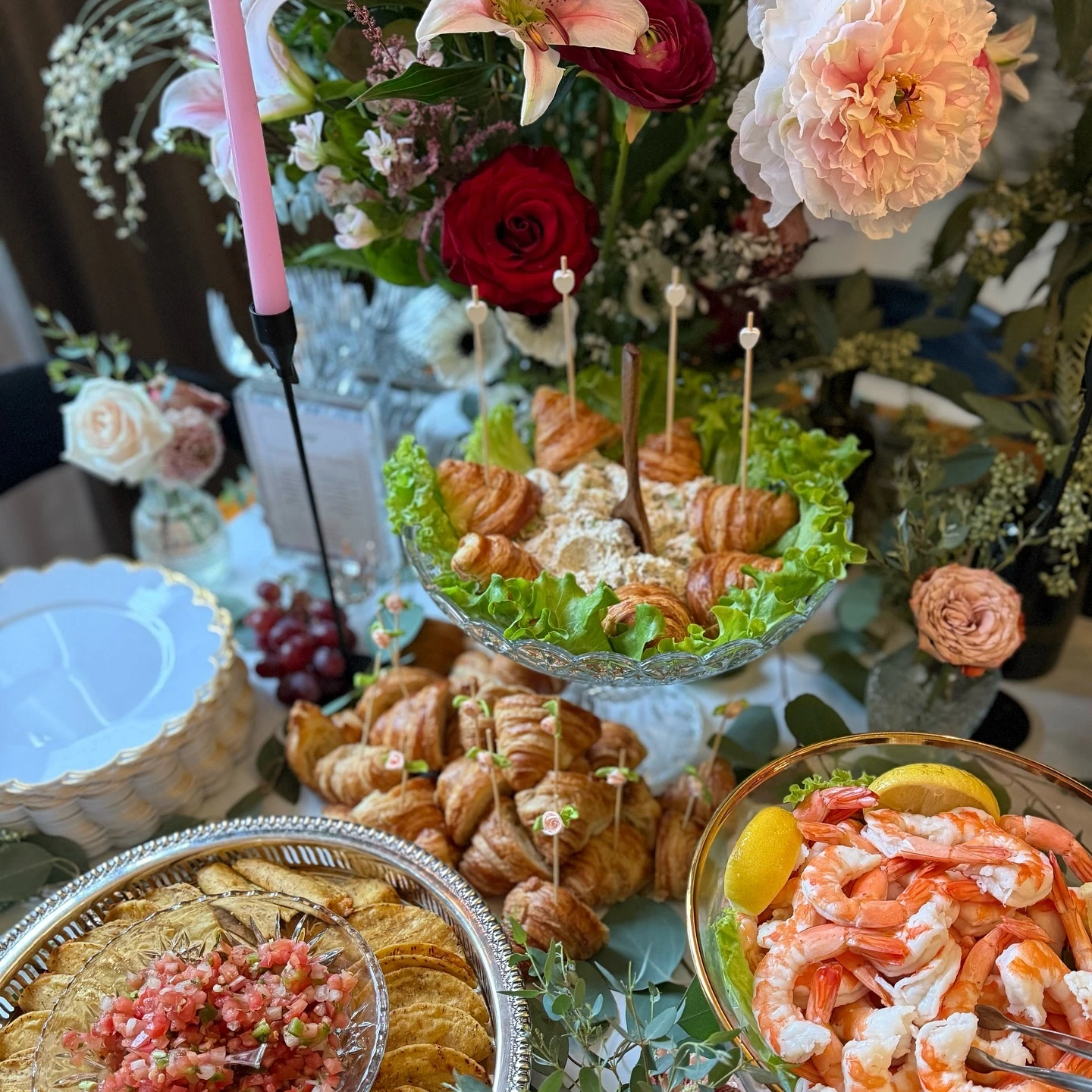 of savory appetizers on a grazing table, including mini croissant sandwiches and shrimp cocktail.