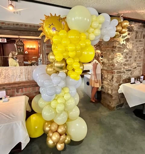 A yellow, white, and gold balloon garland with a smiling sun foil balloon for a sunshine baby shower.
