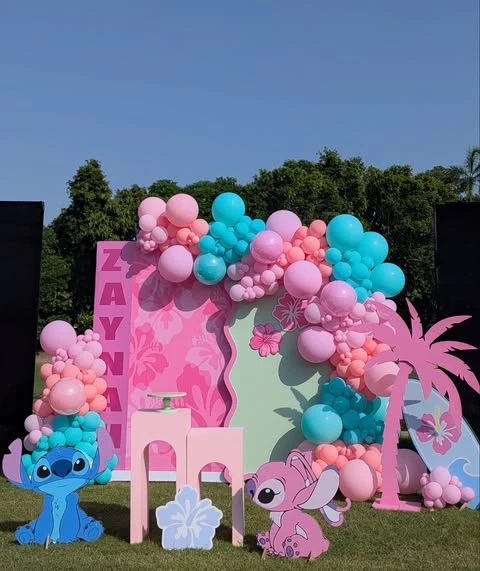 A Stitch and Angel birthday party backdrop with large character cutouts and a pink and teal balloon garland.
