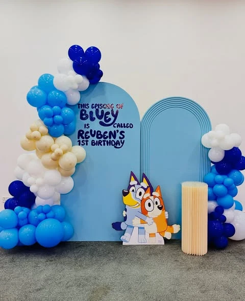 A light blue arched backdrop for a Bluey birthday party, featuring custom text and character cutouts of Bluey and Bingo.