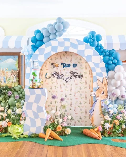 A Peter Rabbit cutout next to a checkered arch backdrop for a baby shower photo zone.