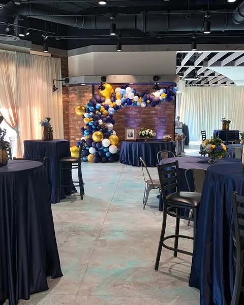 A retirement party venue showing navy tablecloths on all tables, with the main balloon arch visible in the background.
