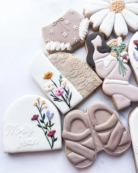 An assortment of wildflower-themed baby shower cookies, including designs with delicate flowers, embossed patterns, and baby sandals.