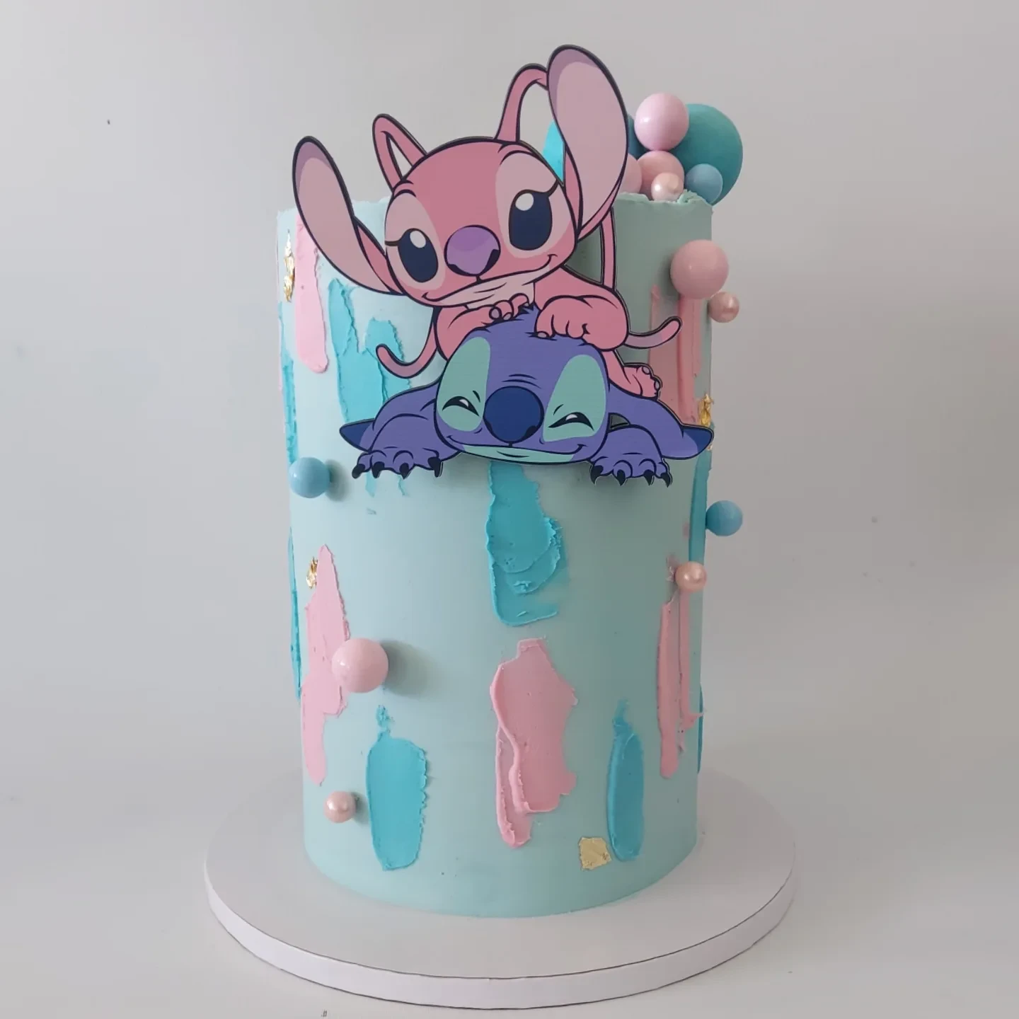A tall modern birthday cake with a Stitch and Angel topper, featuring aqua, pink, and turquoise frosting for a Stitch birthday party.