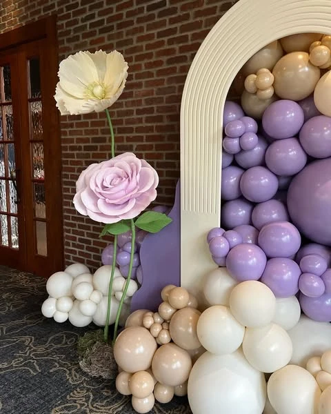 of large, handcrafted paper flowers in pink and cream nestled into a pastel balloon garland.