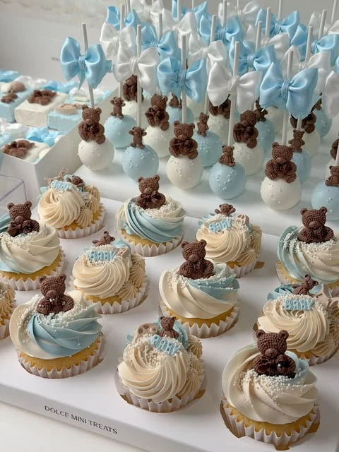 Teddy bear cupcakes with blue and white frosting and cake pops with satin bows.
