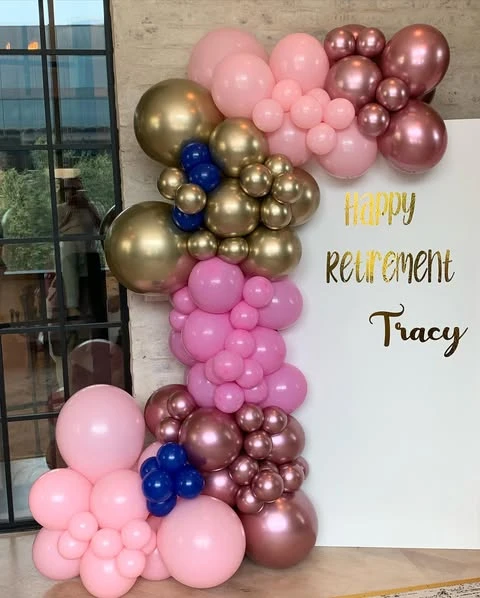 A 'Happy Retirement' party backdrop with a pink, gold, and blue balloon garland.