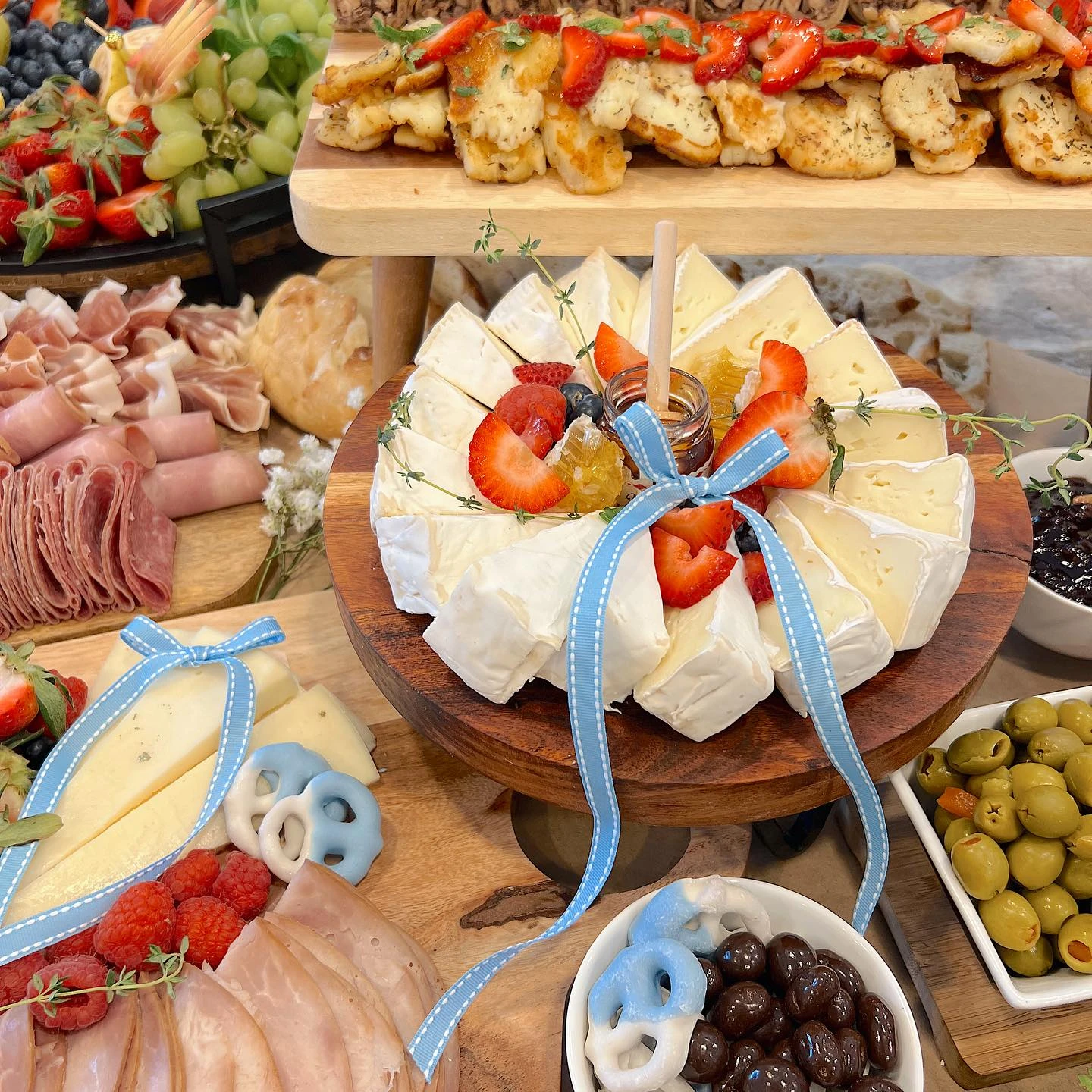A wheel of brie cheese on a wooden stand, cut into wedges and decorated with a blue ribbon and strawberries for a baby shower.