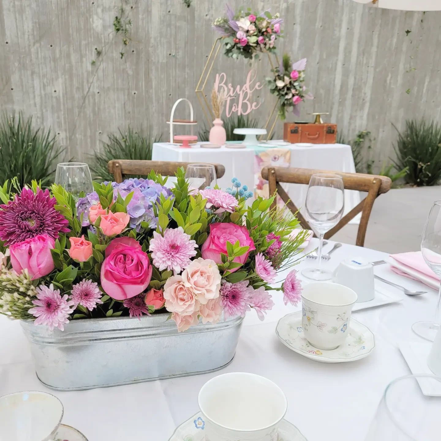 Rustic-chic centerpiece with pink flowers in a galvanized tub on a white tablecloth for a special event.