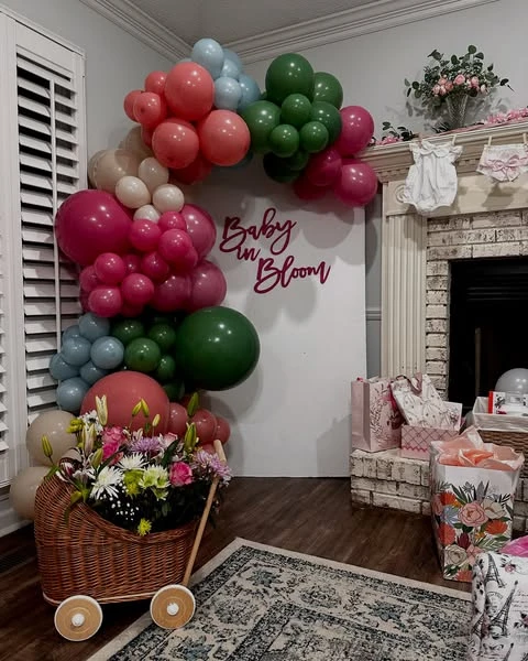 A 'Baby in Bloom' baby shower theme with a wicker pram filled with a bouquet of pink, white, and purple wildflowers next to a white backdrop.