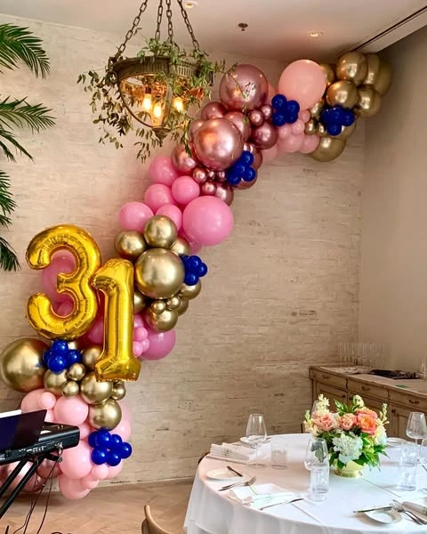 A balloon arch in pink, gold, and blue over a party table, demonstrating a different shape for the decor.