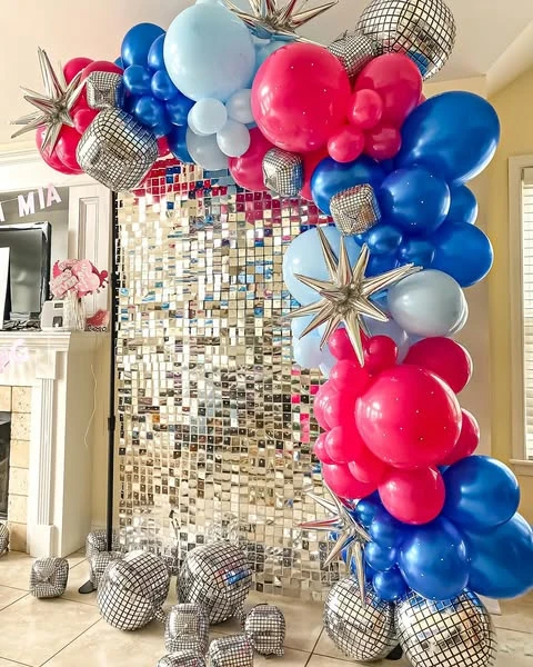A Mamma Mia bachelorette party photo backdrop with a silver shimmer wall and a balloon arch in pink, blue, and silver.