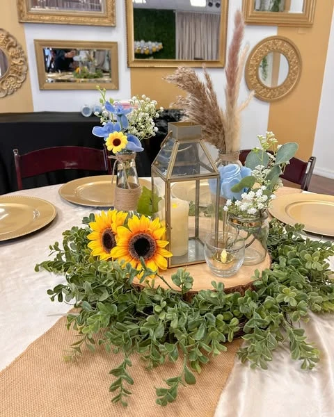 Rustic baby shower centerpiece with a lantern, sunflowers, and a wood slice on a burlap table runner.