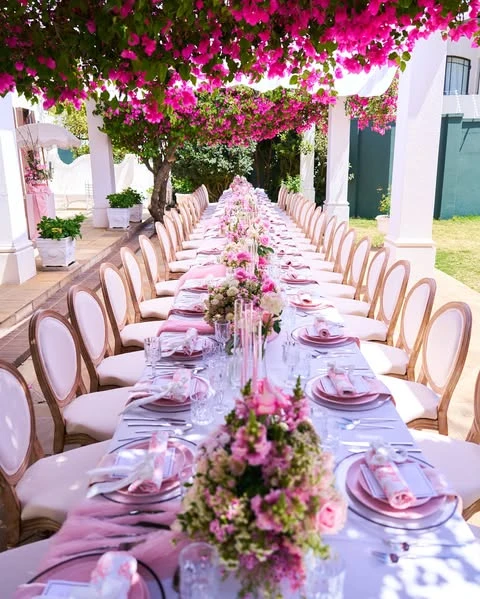 Long, elegant outdoor tablescape for a spring bridal shower under a canopy of pink flowers.