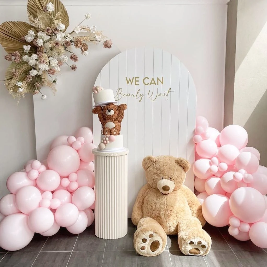 A 'We Can Bearly Wait' baby shower backdrop with pink balloons and a large teddy bear.