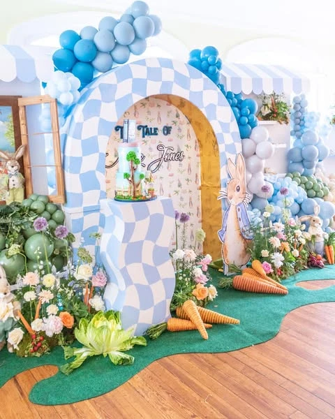 A Peter Rabbit baby shower backdrop grounded with a green grass-like floor mat.