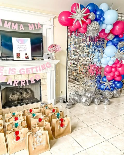 Mamma Mia themed party decor including banners over a fireplace, a balloon arch, and party favor bags.