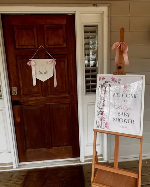 A baby shower welcome sign on a wooden easel, decorated with watercolor wildflowers.