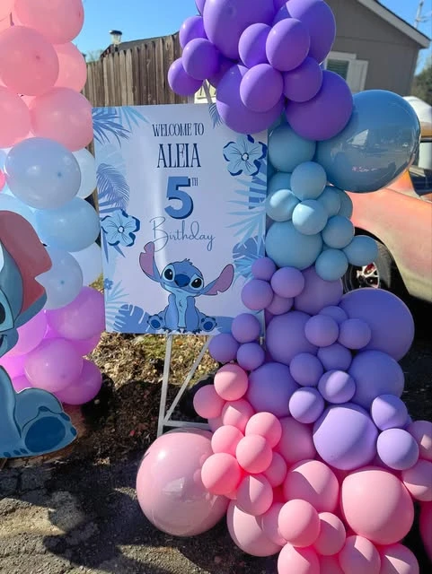 A Stitch-themed birthday party welcome sign on an easel, decorated with a colorful balloon garland.