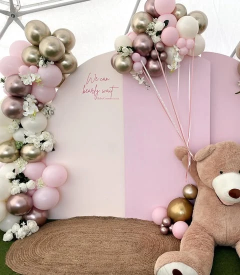 A 'We can bearly wait' baby shower backdrop with pink and metallic balloon garlands.