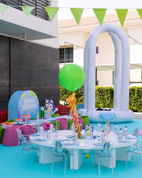 An outdoor Bluey birthday party setup with a dining table and a 'Slime Station' in the background.