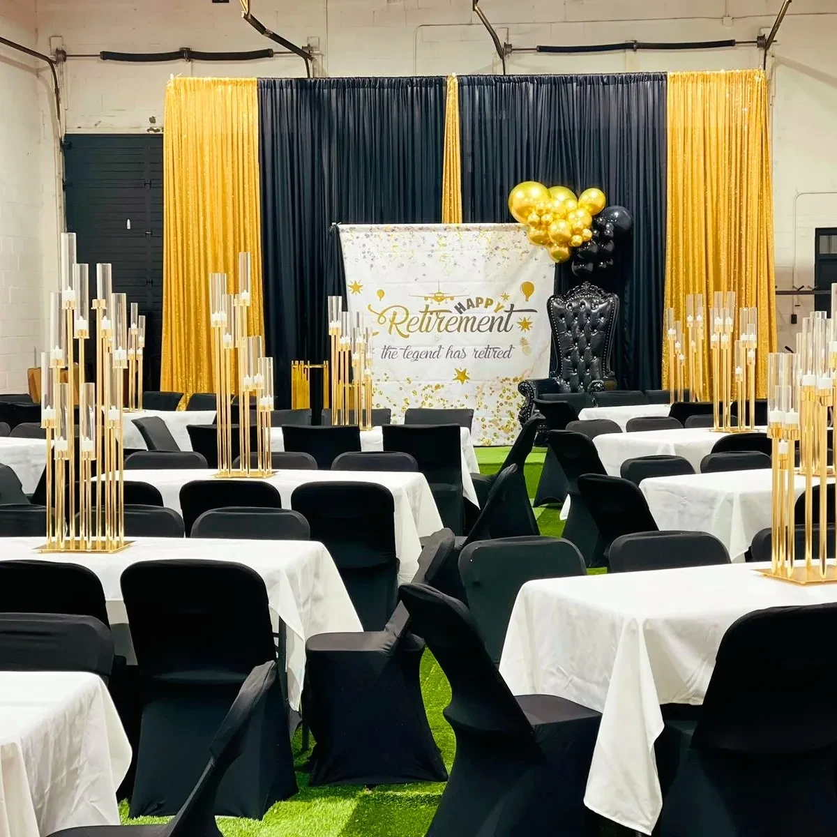 Wide view of a retirement party reception with a black and gold theme, featuring a 'Happy Retirement' backdrop and tables with tall gold centerpieces.