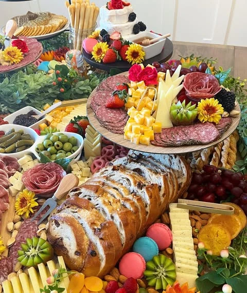 A dense and colorful baby shower grazing table with meats, cheeses, fruits, and a brie wheel cake.