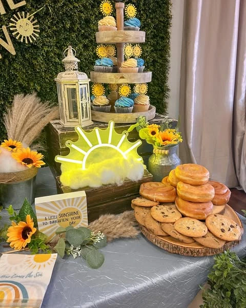 of a dessert table with a cupcake tower, donuts, and a neon sun sign.