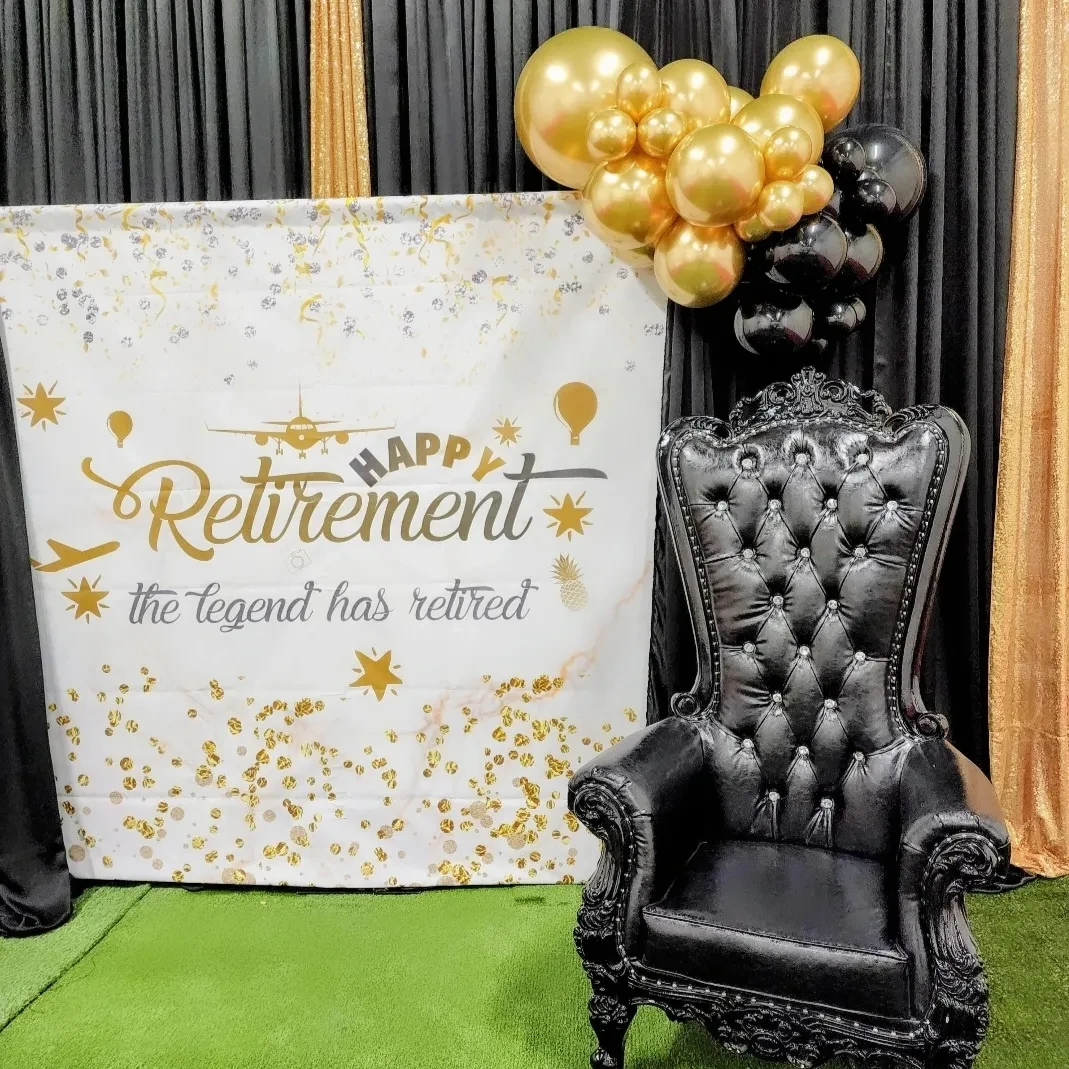 A black tufted throne chair sits next to a 'Happy Retirement' photo backdrop with a small black and gold balloon garland.
