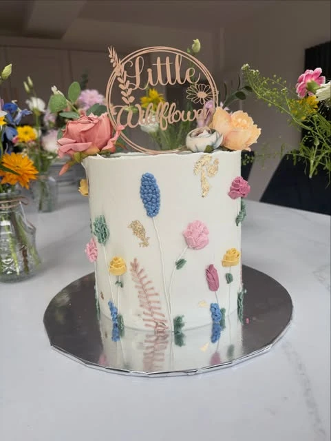 White baby shower cake with a 'Little Wildflower' topper and colorful buttercream flowers.