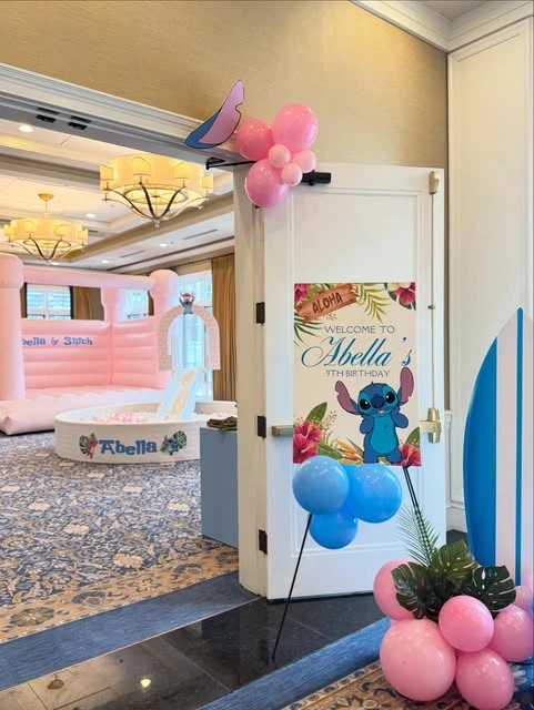 A welcome sign for a Stitch themed birthday party, with a pink bouncy castle in the background.