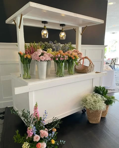 White wooden flower cart filled with pink, orange, and purple spring flowers for a bridal shower.